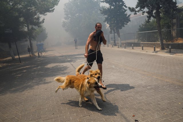 A man, with his dogs, runs as a wildfire burns in the village of Krioneri, north of Athens, Greece on August 6, 2021. (Photo by Costas Baltas/Reuters)