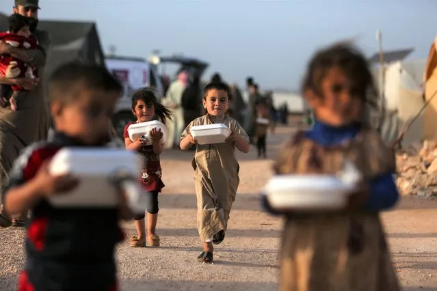 Displaced Syrian children return to their tents with boxes of food distributed by a local charity organisation, before the 'Iftar' meal during the Muslim holy month of Ramadan, at a camp for displaced people on the outskirts of the rebel-held town of Dana, east of the Turkish-Syrian border in the northwestern Idlib province, on April 3, 2022. (Photo by Aaref Watad/AFP)