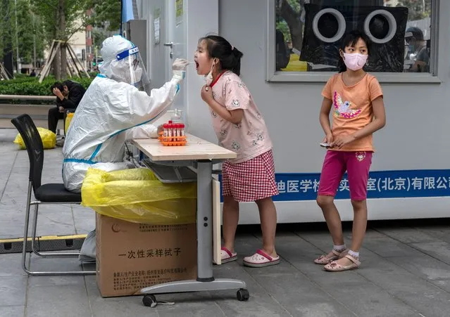A girl is given a nucleic acid test by a health worker, after a recent COVID-19 outbreak, at a testing site on June 14, 2022 in Beijing, China. China's capital is working to control a fresh COVID-19 cluster after dozens of people linked to a local nightclub tested positive for the virus. After easing restrictions earlier in the week, local authorities have initiated local mass testing and targeted lockdowns in addition to mandated proof of a negative PCR test within 72 hours to enter most public spaces and entertainment establishments and bars in some districts have been ordered to close in an effort to maintain the country's zero COVID strategy. (Photo by Kevin Frayer/Getty Images)