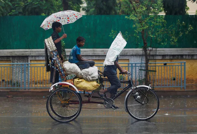 Boys shelter from rain as they travel on a cycle rickshaw in Allahabad, India, June 22, 2016. (Photo by Jitendra Prakash/Reuters)