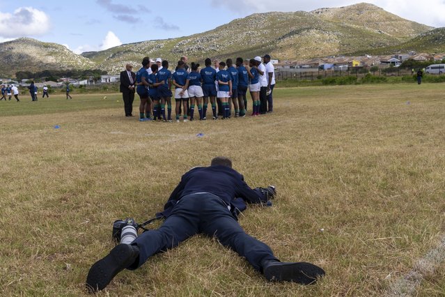 A photographer lies on the ground to take a picture of Britain's Prince William greeting pupils at the Ocean View Secondary School in Cape Town, South Africa, Monday, November 4, 2024. (Photo by Jerome Delay/AP Photo)