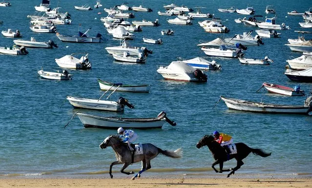 Jockeys race along a beach during the annual beach horse races in Sanlucar de Barrameda near Cadiz on August 25, 2022. While originally the horse races on the beach of Sanlucar de Barrameda were informal competitions of horse owners who used them for fish transport from the old port to the local markets and nearby towns, the first official race organized by the Royal Horse Races Society of Sanlucar was celebrated on August 31, 1845. (Photo by Cristina Quicler/AFP Photo)