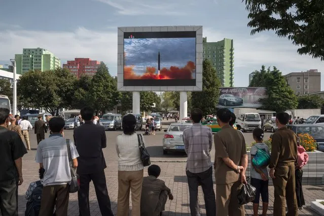 People watch as a screen shows footage of the launch of a Hwasong-12 rocket, beside a billboard advertising North Korea's Pyeonghwa Motors (R), in Pyongyang on September 16, 2017. North Korea said on September 16 it was seeking military “equilibrium” with the United States as leader Kim Jong-Un vowed to complete Pyongyang's nuclear programme. (Photo by Kim Won-Jin/AFP Photo)