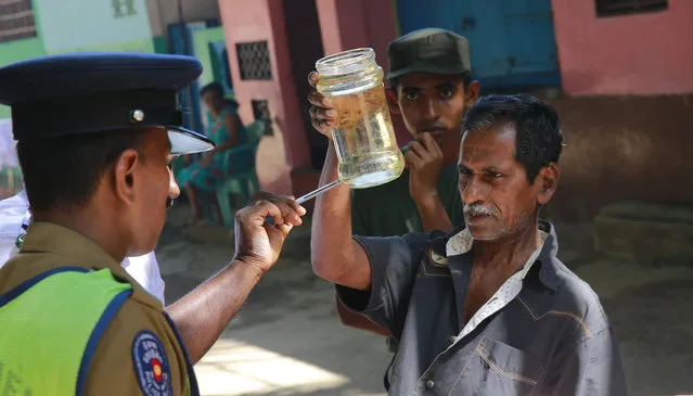 A Sri Lankan public health official,left, points out Mosquito lava in a bottle during a Dengue fever irradiation work in Colombo, Sri Lanka, Tuesday, July 4, 2017. Sri Lanka is suffering its worst dengue outbreak with more than 200 people killed and 76,000 infected this year. Alarmed by the scale of disease, the island nation has deployed hundreds of soldiers and police officers to clear away rotting garbage, stagnant water pools and other potential mosquito-breeding grounds. (Photo by Eranga Jayawardena/AP Photo)
