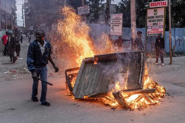 An Azimio la Umoja coalition party supporter protests in front of a burning barricade near Kenyan Police Officers in the informal settlement of Mathare in Nairobi, Kenya, on August 15, 2022. The head of Kenya's election body on August 15, 2022 declared Deputy President William Ruto the winner of the country's close-fought presidential election, despite several commissioners rejecting the results. (Photo by Luis Tato/AFP Photo)