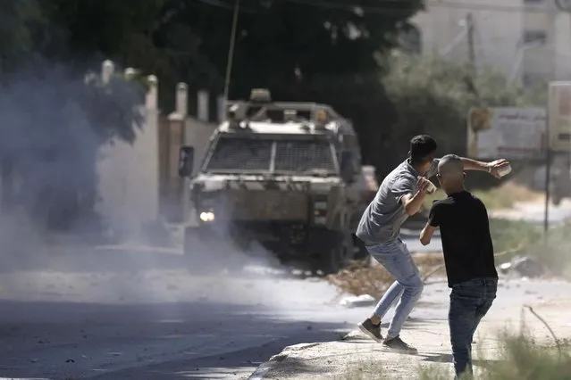 A Palestinian throws stones at an Israeli military vehicle following a deadly raid in the occupied West Bank town of Jenin, Wednesday, September 28, 2022. At least four Palestinians were killed and dozens of others wounded, the Palestinian Health Ministry reported, the latest in a series of deadly Israeli operations in the occupied territory. (Photo by Majdi Mohammed/AP Photo)