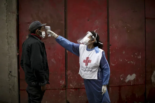 A Red Cross volunteer measures the temperature of man inside the Fraga slum, during a government-ordered lockdown to curb the spread of the new coronavirus, in Buenos Aires, Argentina, Saturday, June 6, 2020. (Photo by Natacha Pisarenko/AP Photo)