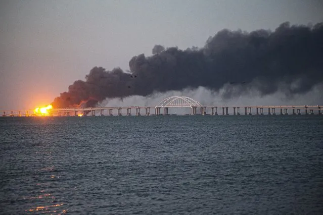 Flame and smoke rise from the Crimean Bridge connecting Russian mainland and the Crimean peninsula over the Kerch Strait, in Kerch, Crimea, Saturday, October 8, 2022. Russian authorities say a truck bomb has caused a fire and the partial collapse of a bridge linking Russia-annexed Crimea with Russia. Three people have been killed. The bridge is a key supply artery for Moscow's faltering war effort in southern Ukraine. (Photo by AP Photo/Stringer)