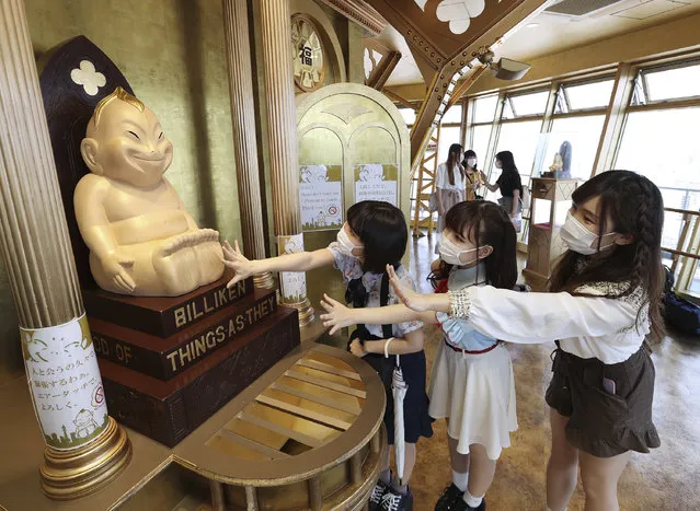 Visitors wearing face masks, amid concerns of the COVID-19 coronavirus, “air touch” the Billiken statue for good luck at the reopened observation deck of Tsutenkaku tower in Osaka on May 30, 2020. (Photo by JIJI Press/AFP Photo/Stringer)