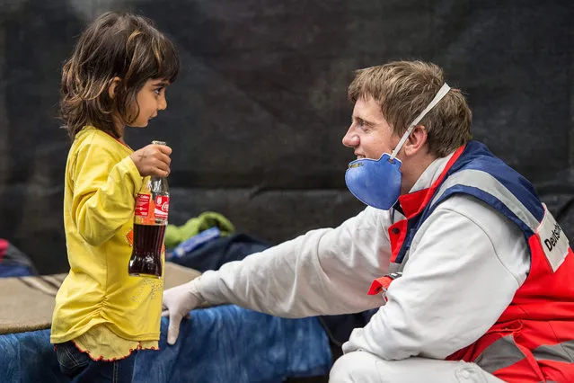 A volunteer from the German Red Cross plays with Zena, a little girl from Syria in an emergerncy shelter in Rottenburg, Germany, 16 September 2015. They are trying to active their German sim cards. In the night some 130 refugees were bought from Essling and a 140 more from Karlsruhe state processing centre were brought to the emergency accommodation. (Photo by Wolfram Kastl/EPA)