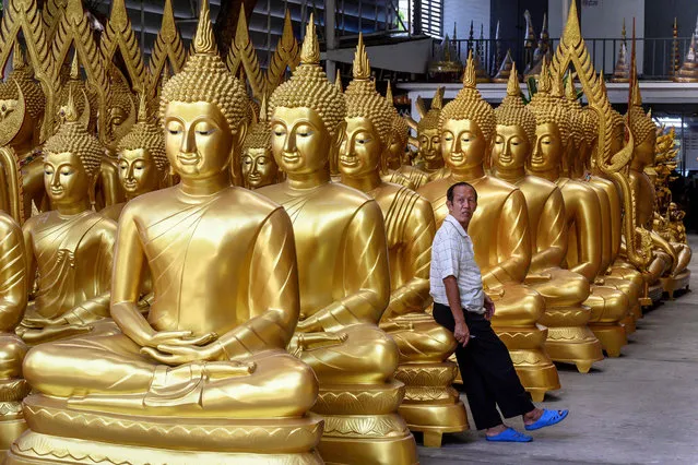 An employee leans on a Buddha statue at a shop selling the Buddhist religious figures in Bangkok on June 10, 2020. (Photo by Mladen Antonov/AFP Photo)