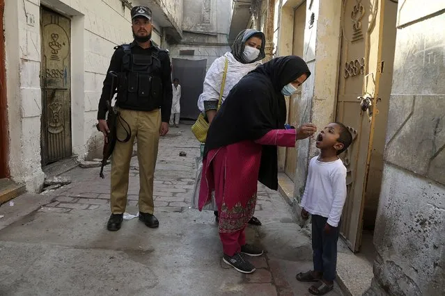 A police officer stands guard while a health worker gives a polio vaccine to a child in Peshawar, Pakistan, Monday, October 24, 2022. (Photo by Muhammad Sajjad/AP Photo)