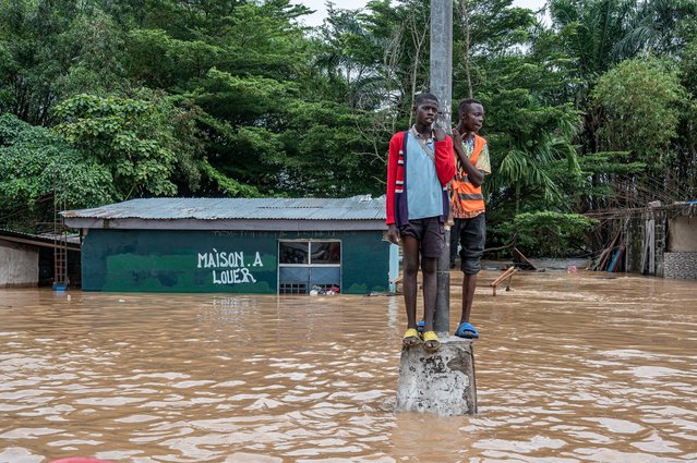 Residents stand on a pole for safety as floodwaters engulf a road following heavy rains in the Ndjili district of Kinshasa on April 6, 2025. (Photo by Hardy Bope/AFP Photo)