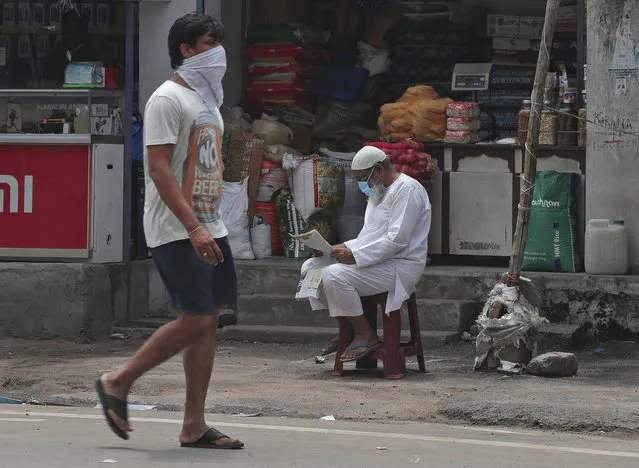 A man walks past a vendor reading a newspaper in Hyderabad, India, Saturday, July 11, 2020. (Photo by Mahesh Kumar A./AP Photo)