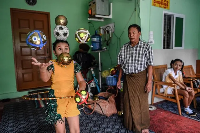 This photograph taken on July 5, 2022 shows septuagenarian Ohn Myint (C) keeping watch on a performing youth as his granddaughter Han Myint Mo (L) looks on during a juggling training session at a residence in Yangon. Han Myint Mo kicks up a gold-coloured metal ball, pirouettes and catches it on the blade of a knife held in her teeth – keeping up a Myanmar juggling tradition on the edge of extinction. (Photo by AFP Photo/Stringer)