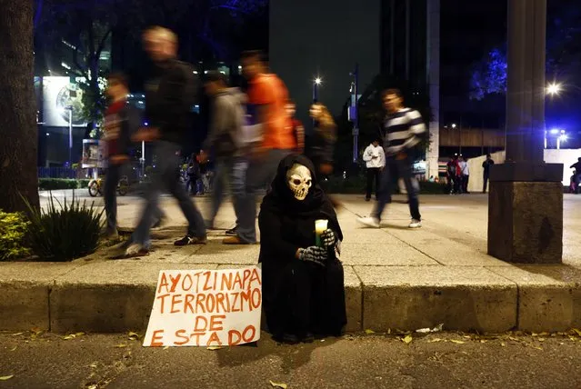 A person in a disguise sits on a sidewalk holding a candle during a protest denouncing the apparent massacre of 43 trainee teachers in Mexico City late November 8, 2014. Protesters tried to set the wooden door of Mexican President Enrique Pena Nieto's ceremonial palace on fire in the historic center. (Photo by Edgard Garrido/Reuters)