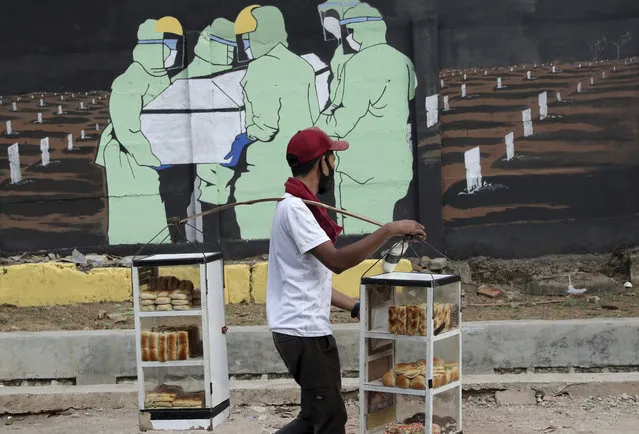 A bread vendor passes by a coronavirus-themed mural in Jakarta, Indonesia, Thursday, Sepember 10, 2020. Jakarta's governor announced an emergency decision on Wednesday to reimpose large-scale social restrictions in the capital city to control a rapid expansion in coronavirus cases. (Photo by Tatan Syuflana/AP Photo)