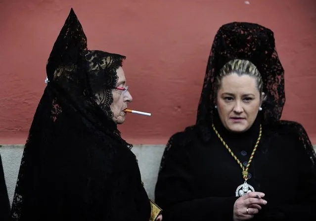 Women wearing traditional mantilla dresses smoke outside a church before taking part in the Brotherhood procession of “Los Estudiantes” (“The Students”) at the start of Holy Week in Oviedo, Spain, on March 24, 2013. (Photo by Eloy Alonso/Reuters)