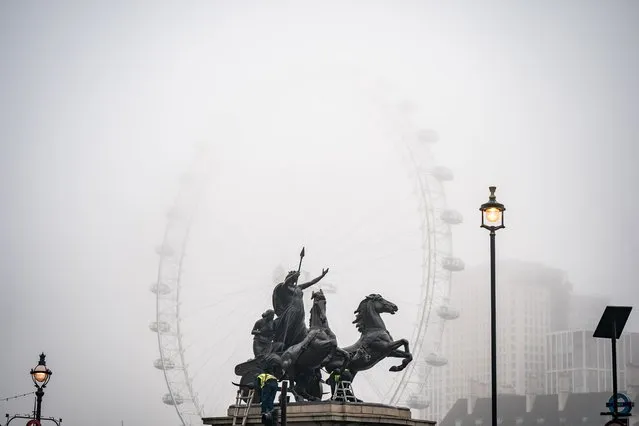 Workers clean the Boudiccan Rebellion statue on the Victoria Embankment whilst fog surrounds the lastminute.com London Eye, on the South Bank of the River Thames, in London on Wednesday, January 25, 2023. (Photo by Aaron Chown/PA Images via Getty Images)