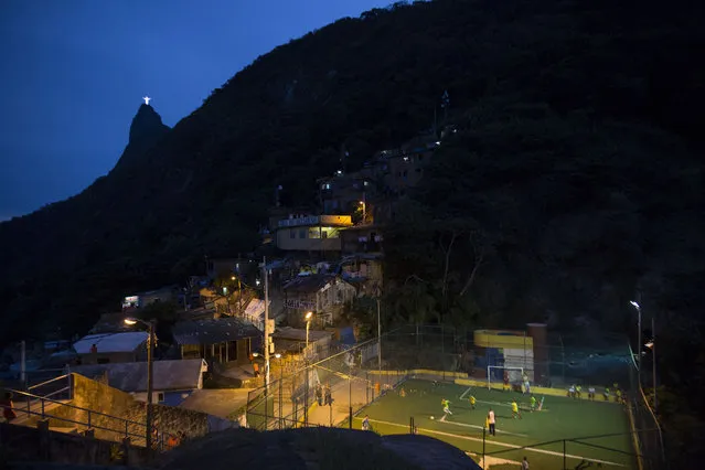In this June 6, 2014 file photo, people play soccer in the Dona Marta slum, backdropped by the Christ the Redeemer statue and Corcovado Mountain in Rio de Janeiro, Brazil. Soccer schools operate in nearly all of the slums, from the Dona Marta shantytown, which is ensconced in the middle-class Botafogo neighborhood, to Mangueira, a historic slum overlooking the mythical Maracana Stadium. (Photo by Felipe Dana/AP Photo)
