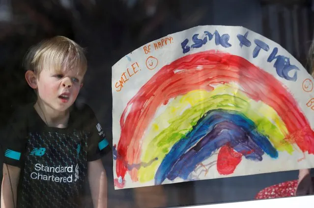Theo Clay looks out of his window next to his hand-drawn picture of a rainbow in Liverpool, as the spread of coronavirus disease (COVID-19) continues. Liverpool, Britain, March 25, 2020. (Photo by Phil Noble/Reuters)