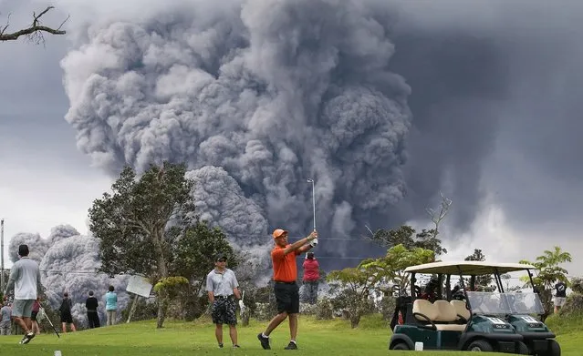 People play golf as an ash plume rises in the distance from the Kilauea volcano on Hawaii's Big Island on May 15, 2018 in Hawaii Volcanoes National Park, Hawaii. The U.S. Geological Survey said a recent lowering of the lava lake at the volcano's Halemaumau crater 'has raised the potential for explosive eruptions' at the volcano. (Photo by Mario Tama/Getty Images)