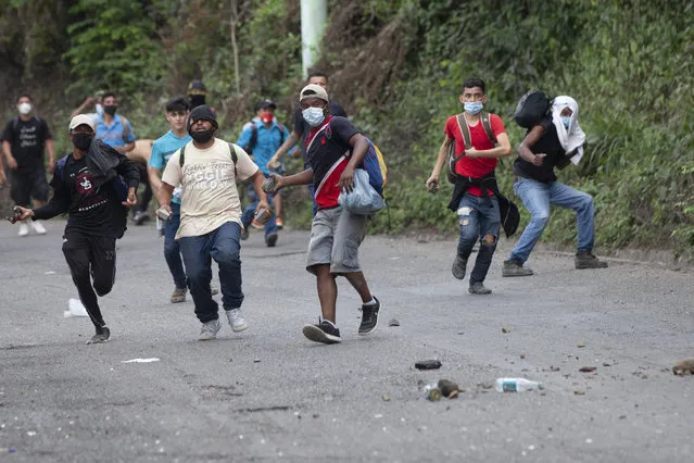 Honduran migrants throw stones toward Guatemalan soldiers and police blocking them from advancing toward the US, on the highway in Vado Hondo, Guatemala, Monday, January 18, 2021. The roadblock was strategically placed at a chokepoint on the two-lane highway flanked by a tall mountainside and a wall leaving the migrants with few options. (Photo by Sandra Sebastian/AP Photo)