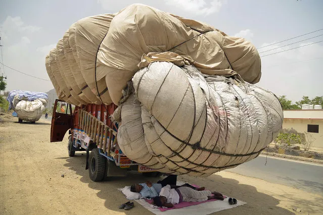 Indian men sleep in the shadow of an overflowing cloth container of hay, to be used as animal fodder, on a truck on a hot summer day in Ajmer in the western state of Rajasthan on May 30, 2018. (Photo by Shaukat Ahmed/AFP Photo)