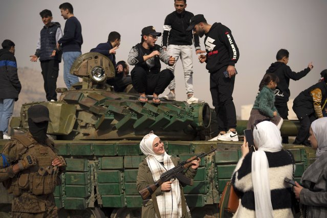 A woman holding a rifle borrowed from a Syrian opposition fighter poses for a picture, next to a government forces tank that was left on a street, at the Umayyad Square in Damascus, Syria, Wednesday, December 11, 2024. (Photo by Leo Correa/AP Photo)