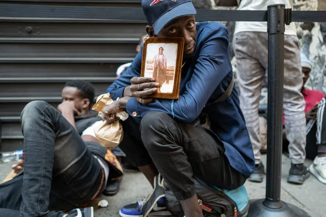 A man from Senegal holds up a religious book with a picture of a West African sheikh on the cover as he joins hundreds of recently arrived migrants to New York City outside of the Roosevelt Hotel, which has been made into a reception center, as they try to secure temporary housing on July 31, 2023 in New York City. The migrants, many from Central America and Africa, have been sleeping on the streets or at other shelters as the city continues to struggle with the influx of migrants whose numbers have surged this spring and summer. (Photo by Spencer Platt/Getty Images/AFP Photo)