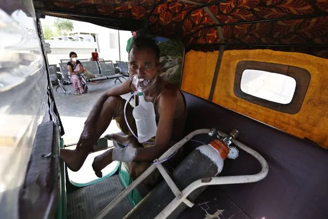 A COVID-19 patient breathes with the help of an oxygen mask as he waits inside an auto rickshaw to be attended to and admitted in a dedicated COVID-19 government hospital in Ahmedabad, India, Thursday, April 22, 2021. Indian authorities scrambled Saturday to get oxygen tanks to hospitals where COVID-19 patients were suffocating amid the world’s worst coronavirus surge, as the government came under increasing criticism for what doctors said was its negligence in the face of a foreseeable public health disaster. (Photo by Ajit Solanki/AP Photo)
