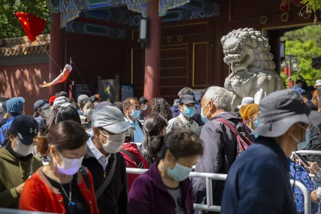 Visitors wearing face masks wait in line to enter a public park in Beijing, Saturday, May 1, 2021. Chinese tourists are expected to make a total of 18.3 million railway passenger trips on the first day of the country's five-day holiday for international labor day, according to an estimate by the state railway group, as tourists rush to travel domestically after the coronavirus has been brought under control in China. (Photo by Mark Schiefelbein/AP Photo)