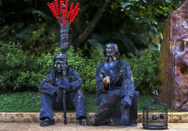 Street artists dressed as bronze statues smokes as he sits next to his partner during a break in their performance in Kunming, Yunnan province, on October 1, 2013. (Photo by Wong Campion/Reuters)