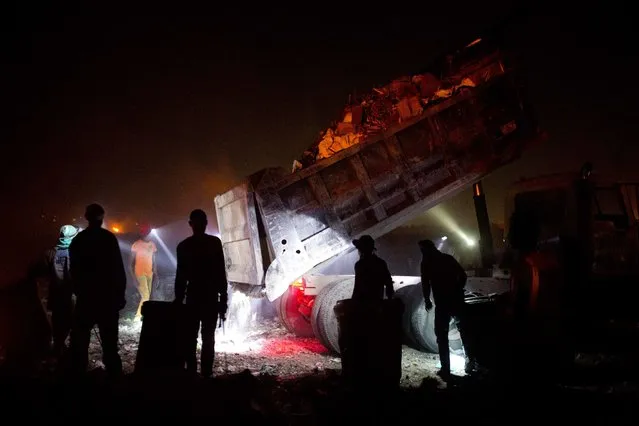 In this August 30, 2018 photo, people who scavenge the trash for valuables use headlamps at night as a truck prepares to dump its load at the Truitier landfill in the Cite Soleil slum of Port-au-Prince, Haiti. Rene Phanor, a slum resident, says pickers often suffer from chronic respiratory illnesses, headaches and infections contracted from used syringes. (Photo by Dieu Nalio Chery/AP Photo)