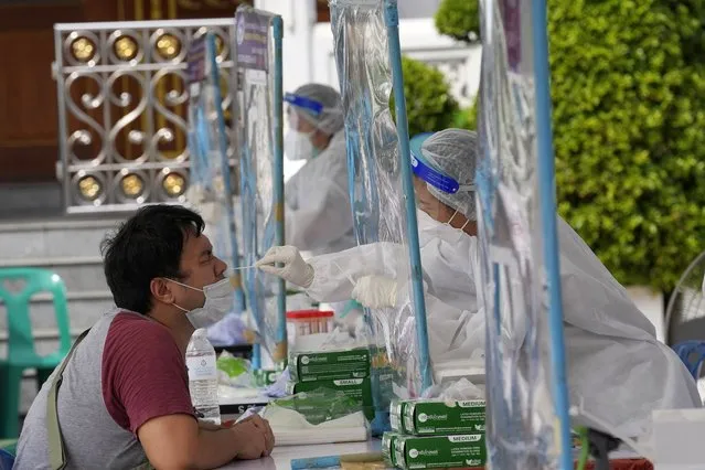 A health worker collects a nasal swab from a local resident for the coronavirus testing at Ratchasingkhon temple in Bangkok, Thailand, Wednesday, July 7, 2021. (Photo by Sakchai Lalit/AP Photo)