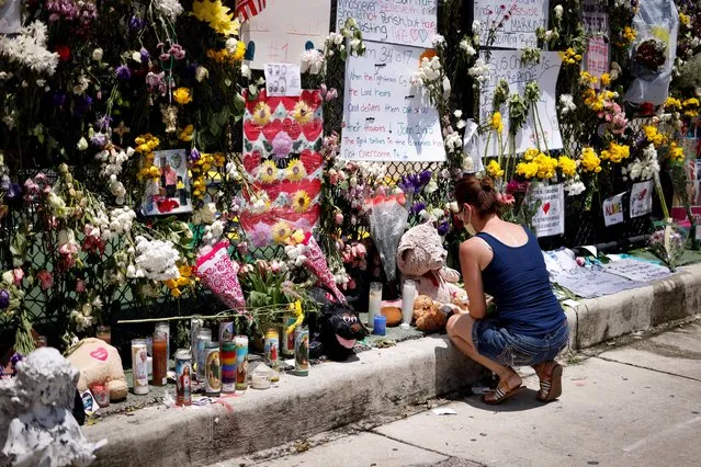 A woman kneels at a memorial site created by neighbors in front of a partially collapsed residential building as the emergency crews continue the search and rescue operations for survivors, in Surfside, Florida, U.S. July 3, 2021. (Photo by Marco Bello/Reuters)