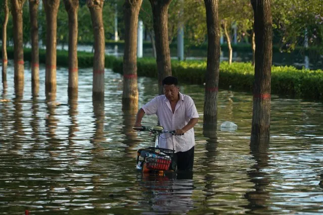 A man pushes a scooter through floodwaters in Xinxiang in central China's Henan Province, Monday, July 26, 2021. Forecasters Monday said more heavy rain is expected in central China's flood-ravaged Henan province, where the death toll continues to rise after flash floods last week that killed dozens of people. (Photo by Dake Kang/AP Photo)