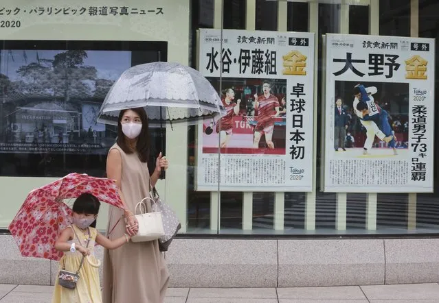 People wearing face masks to protect against the spread of the coronavirus walk past extra papers reporting on Japanese gold medalists at Tokyo Olympics, in Tokyo Tuesday, July 27, 2021. (Photo by Koji Sasahara/AP Photo)