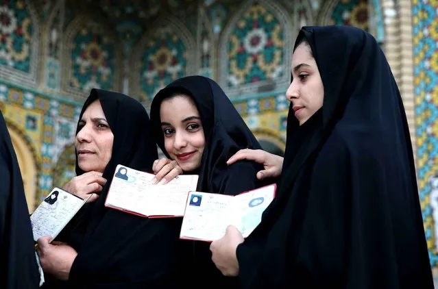 Iranian women show their identification, as they queue in a polling station to vote for the parliamentary and Experts Assembly elections in Qom, 125 kilometers (78 miles) south of the capital Tehran, Iran, Friday, February 26, 2016. Iranians across the Islamic Republic voted Friday in the country's first election since its landmark nuclear deal with world powers, deciding whether to further empower its moderate president or side with hard-liners long suspicious of the West.  (Photo by Ebrahim Noroozi/AP Photo)