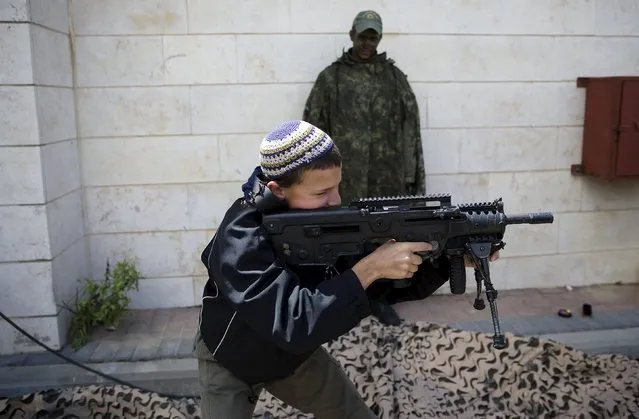 An Israeli boy plays with a rifle during a display of the Israeli Defense Forces (IDF) equipment and abilities at the West Bank settlement of Kiryat Arba, April 23, 2015, during celebrations for Israel's Independence Day, marking the 67th anniversary of the creation of the state. (Photo by Ronen Zvulun/Reuters)