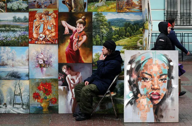 A seller of paintings smokes next to his wares at the Arbat street in central Moscow, Russia, 26 February 2019. (Photo by Yuri Kochetkov/EPA/EFE)