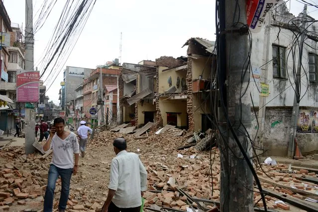 Nepalese people walk past collapsed buildings at Lalitpur, on the outskirts of Kathmandu on April 25, 2015.  A powerful 7.9 magnitude earthquake struck Nepal, causing massive damage in the capital Kathmandu with strong tremors felt across neighbouring countries. (Photo by Prakash Mathema/AFP Photo)