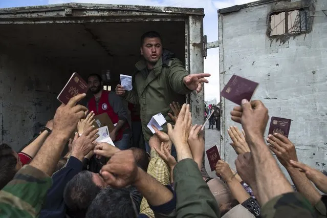 Turkmen people reach out showing their Syrian passports to receive humanitarian aid from the Syrian Arab Red Crescent in Al-Issawiyah, about 15 kilometers of Turkish border, Syria, Friday, March 4, 2016. (Photo by Pavel Golovkin/AP Photo)