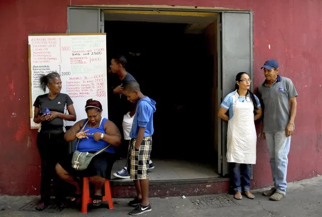 Workers and neighbors stand outside a grocery shop in Caracas, Venezuela, Tuesday, March 26, 2019. Much of Venezuela remains without electricity as a new power outage spread across the country. (Photo by Natacha Pisarenko/AP Photo)