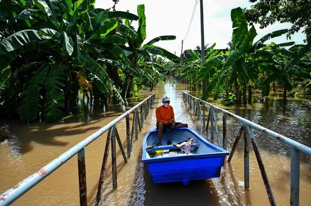 A resident steers his boat over a footbridge through a flooded neighborhood in the central Thai province of Ayutthaya on September 28, 2021, as tropical storm Dianmu caused flooding in 30 provinces across the country. (Photo by Lillian Suwanrumpha/AFP Photo)