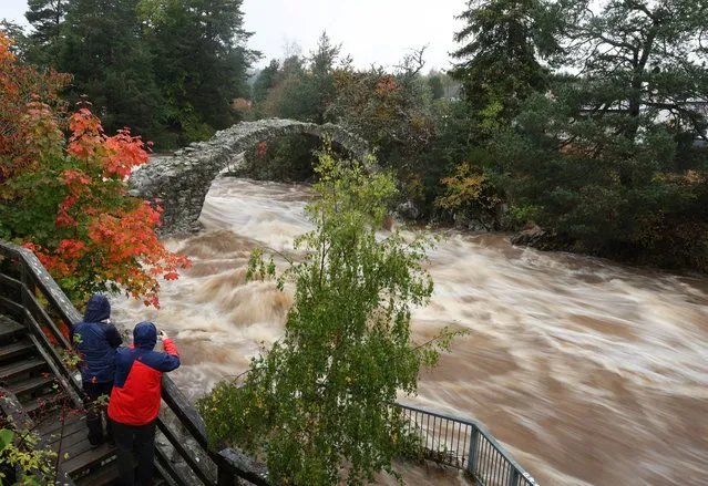 People take pictures as water rushes under the oldest stone bridge in the Highlands at Carrbridge, Scotland, Britain on October 8, 2023. (Photo by Russell Cheyne/Reuters)