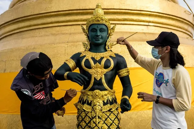 Painters touch up a statue with gold paint at the Wat Saket Buddhist temple in Bangkok on November 9, 2021. (Photo by Jack Taylor/AFP Photo)