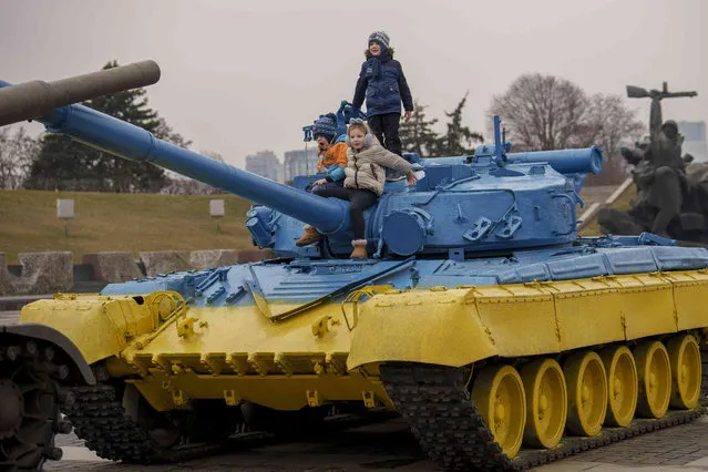 Children play on a tank painted in the colors of the Ukrainian flag, back dropped by the Motherland Monument, in Kyiv, Ukraine, Friday, March 15, 2024. A Russian ballistic missile attack blasted homes in the southern Ukrainian city of Odesa on Friday, followed by a second missile that targeted first responders who arrived at the scene, according to officials who said that at least 16 people were killed. (Photo by Vadim Ghirda/AP Photo)