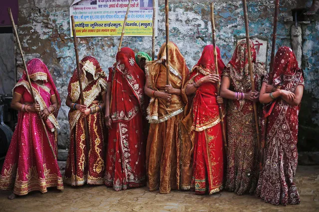 Indian women from Nandgaon village hold wooden sticks as they wait for the arrival of men from Barsana, during Lathmar Holi festival at Nandgaon 120 kilometers (75 miles) south of New Delhi, India, Monday, March 10, 2014. According to a tradition which has its roots in Hindu mythology, men from nearby Barsana village are soaked in colored water by men and beaten with sticks by women as they arrive at Nandgaon, believed to be Lord Krishna's village. (Photo by Altaf Qadri/AP Photo)