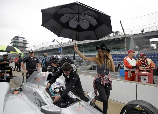 A crewman assists James Jakes, of England, out of the car under an umbrella held by Meghan Williams as rain halted qualifications on the first day of qualifications for the Indianapolis 500 auto race at Indianapolis Motor Speedway in Indianapolis, Saturday, May 16, 2015. (Photo by Darron Cummings/AP Photo)